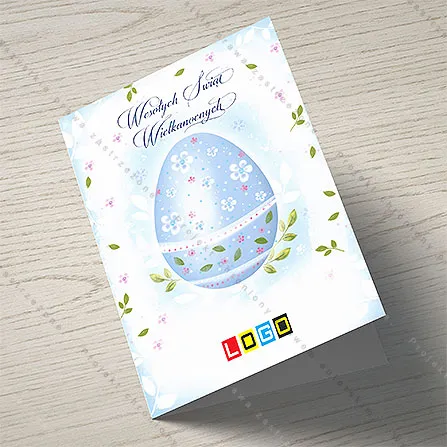 Błękitne jajo z zielonym pasem listków i białymi kwiatkami w górnej części, tło jasnoniebieskie w kropki, nad nim napis