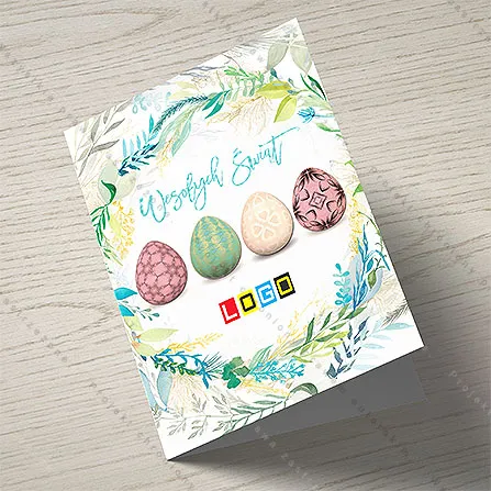 Rząd czterech pastelowych jaj otoczony malowanym wiankiem z liści, powyżej turkusowy napis życzeń na białym tle