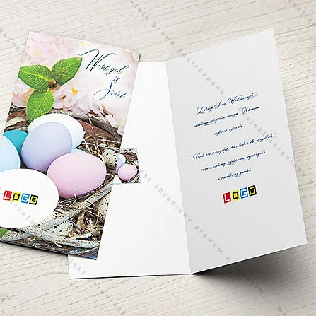 Słomiane gniazdo z jajkami w pastelowych barwach przed rozmytymi różowymi kwiatami, w rogu pionowy niebieski napis